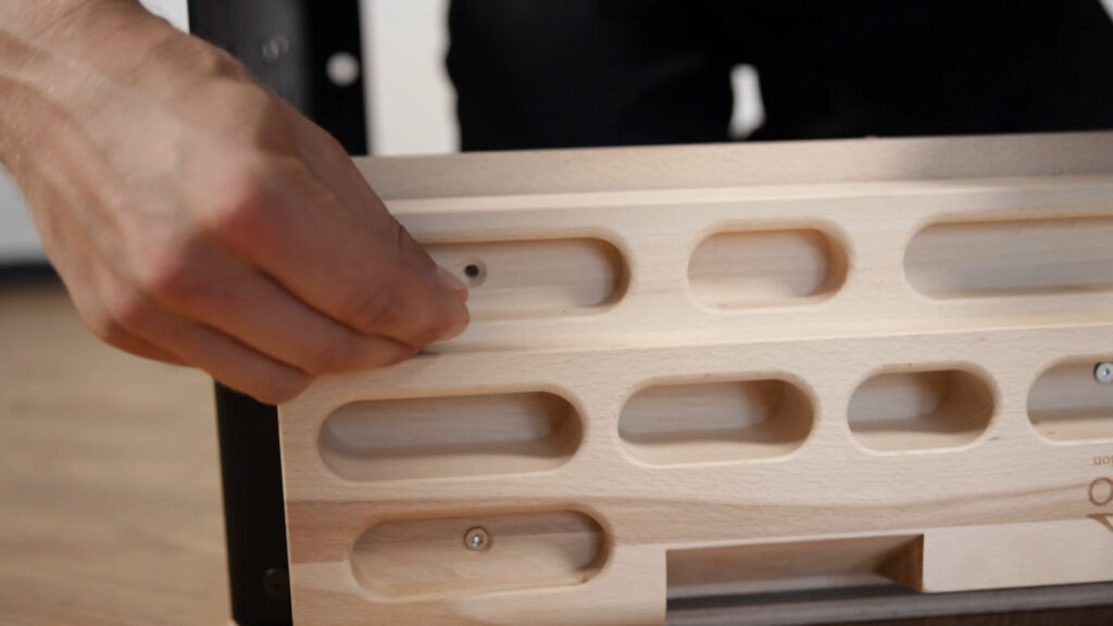 Close up of the hangboard being installed on the clevo wall pull-up bar with a screw being installed.