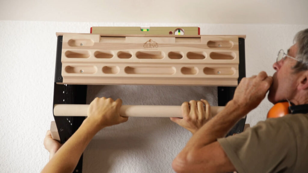 Man checking the spirit level on top of the clevo wall pull-up bar which is held against the wall by two other people.