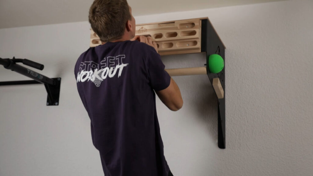 Jelle performs a narrow pull up on the clevo wall pull-up bar using one of the finger cutouts of the hangboard.