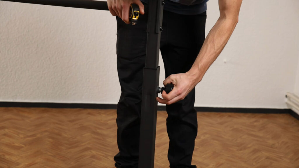 Man in black jogging trousers pulling on the knob on the side of the Gravity Fitness Static Bar to adjust its height.