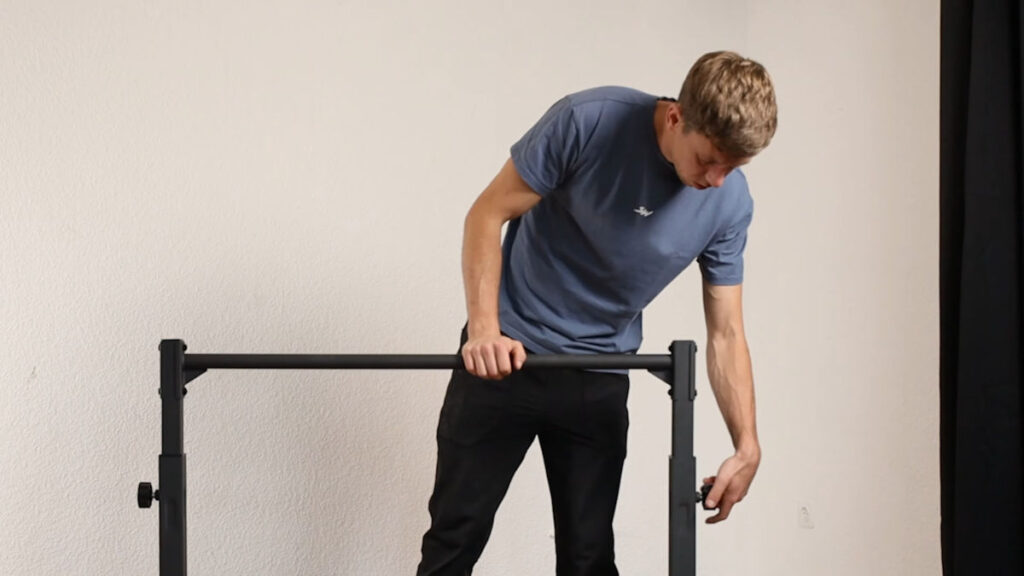 Man in blue tshirt turning the knob on the side of the Gravity Fitness Static Bar to fasten the top bar after having adjust its height.