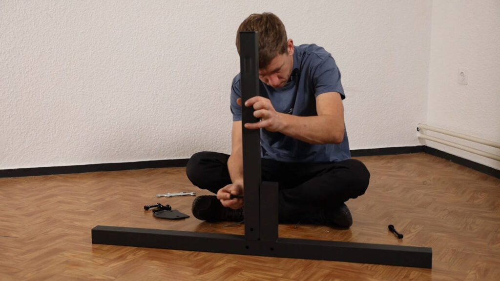 Man in blue tshirt combinging the vertical post with the foot of the Gravity Fitness Static Bar with a large bolt.