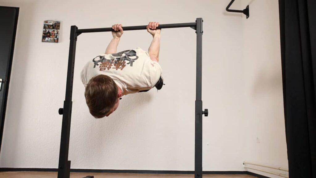 Man in beige tshirt with Japanese lettering performing a back lever under the Gravity Fitness Static Bar.