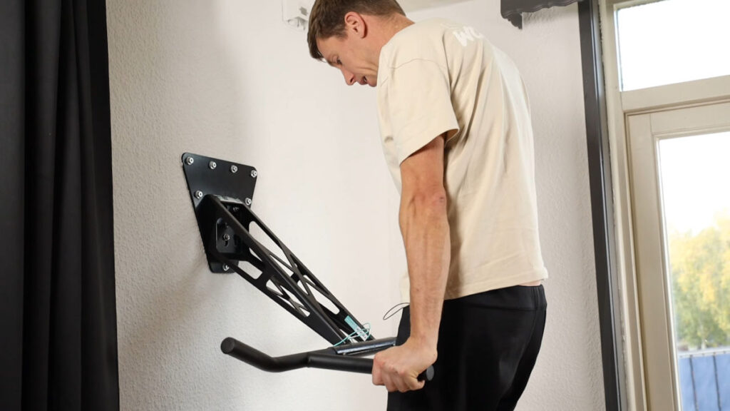 Man in white shirt performing a dip on the Mobile Pullup and Dip Bar in a white room with outside looking windows.