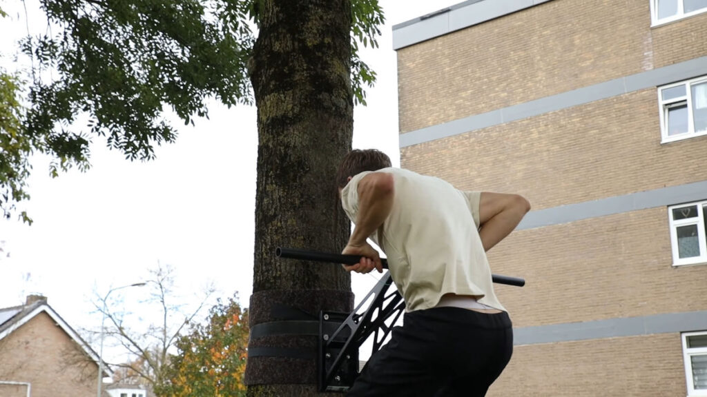 Man in white shirt performing a muscle-up on the Mobile Pullup and Dip Bar mounted to a tree outside.