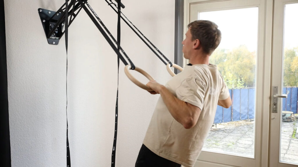 Man in white shirt using Gymnastic Rings to perform rows with the rings attached to the Pullup and Dip Bar.