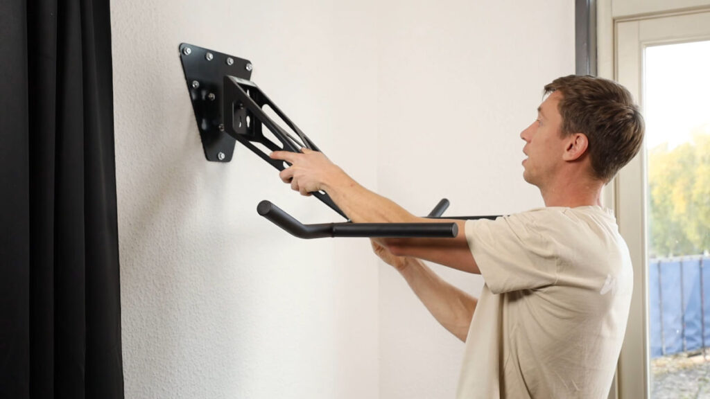 Man in white shirt inserting the Pullup and Dip Bar onto its base plate in the dip configuration.