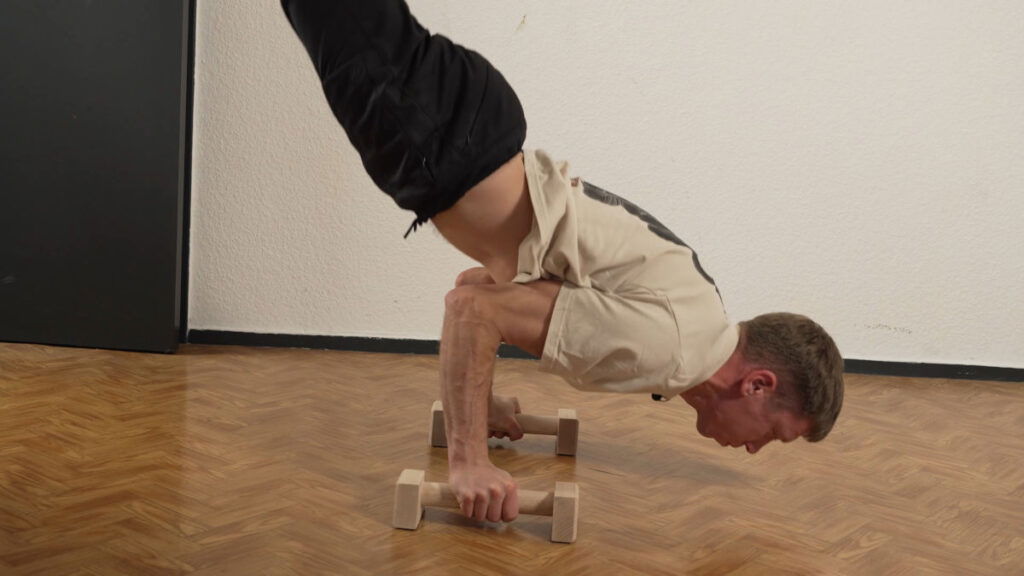 Man in white shirt performs a handstand push up on the Caliathletic mini parallettes.