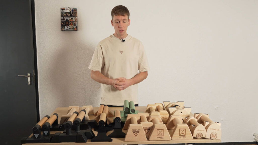 Man in white shirt standing in front of table filled with Mini Parallettes.