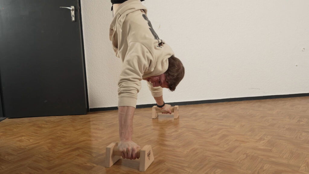 Man in white shirt performing a wide handstand with difficulty on the Pullup and Dip Premium parallettes.