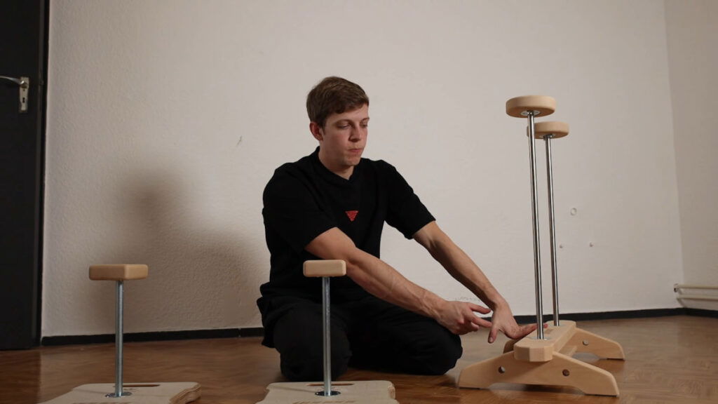 Man in black shirt sitting between the Compact and Elite Gorletic Handstand Canes, touching the base of the Elite Gorletic Handstand Canes.