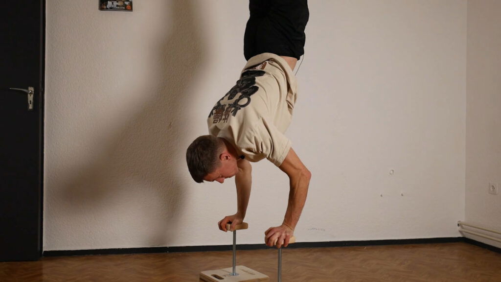 Man in white shirt performing a handstand on the Compact Gorletic Handstand Canes.