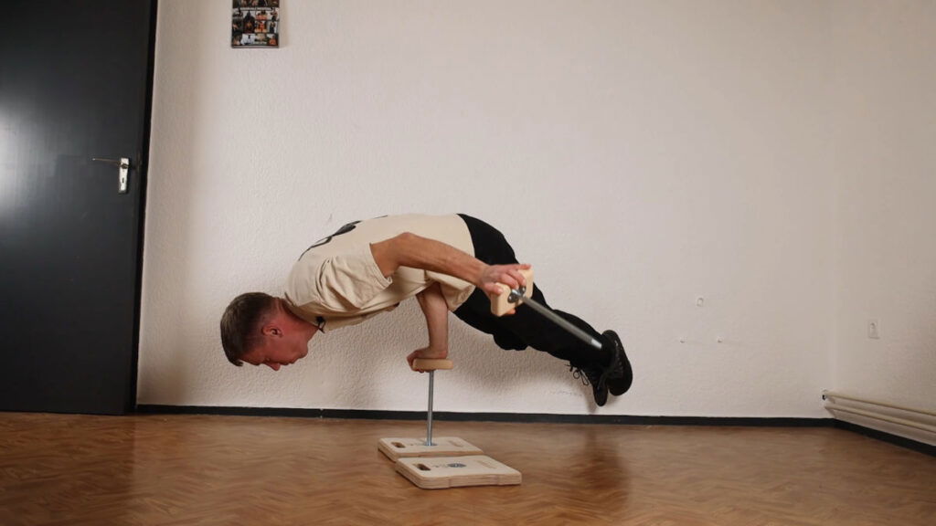 Man in white shirt performing a one-arm planche on the Compact Gorletic Handstand Canes while holding the cane on the offhand up in the air.