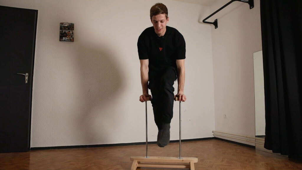 Man with black shirt performing a straight arm plank prior to moving into an L-sit on the Elite Gorletic Handstand Canes.