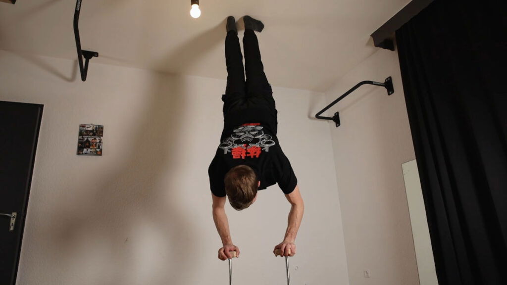 Man in black shirt with Japanese symbols on it performing a handstand on the Elite Gorletic Handstand Canes.