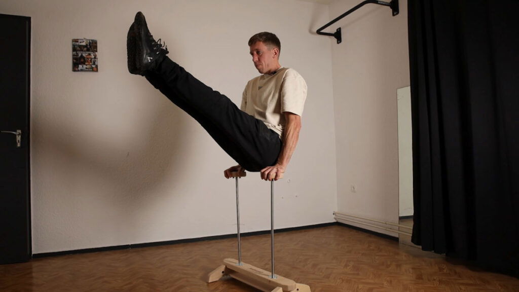 Man in white shirt and black trousers performing a v-sit exercise on the Elite Gorletic Handstand Canes.