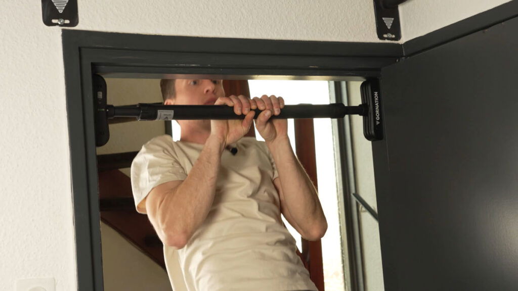 Man in white shirt performing a narrow Pull-Up on the Gornation Pull-Up Bar "Extend-It" in a doorway.