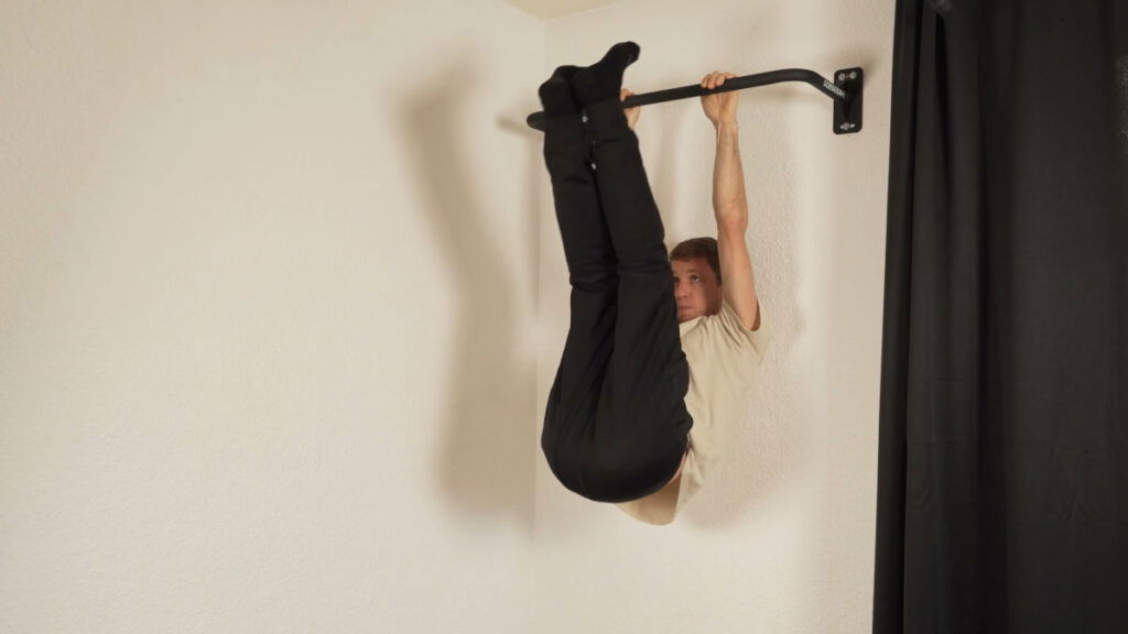 Man in white shirt performing a full leg raise on the Gornation Pull-Up Bar "Multi" mounted on a white wall.