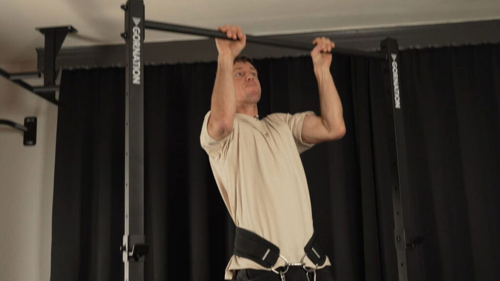 Man in white shirt wearing a Dip Belt performing weighted Pull-Ups on the Gornation Pull-Up Station.