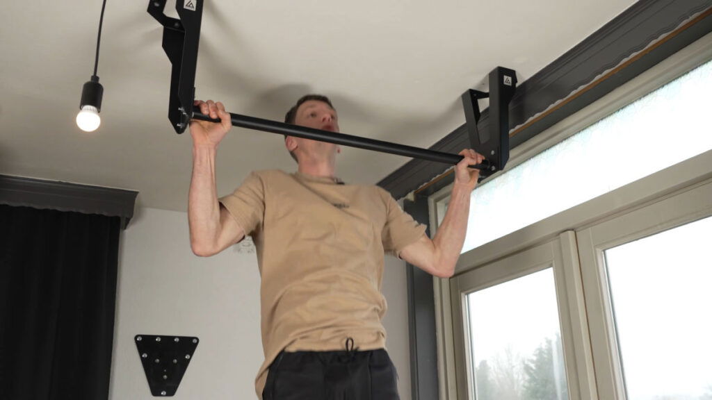 Man in beige shirt performing a full range of motion Pull-Up on the Caliathletics Ceiling Pull-Up Bar.