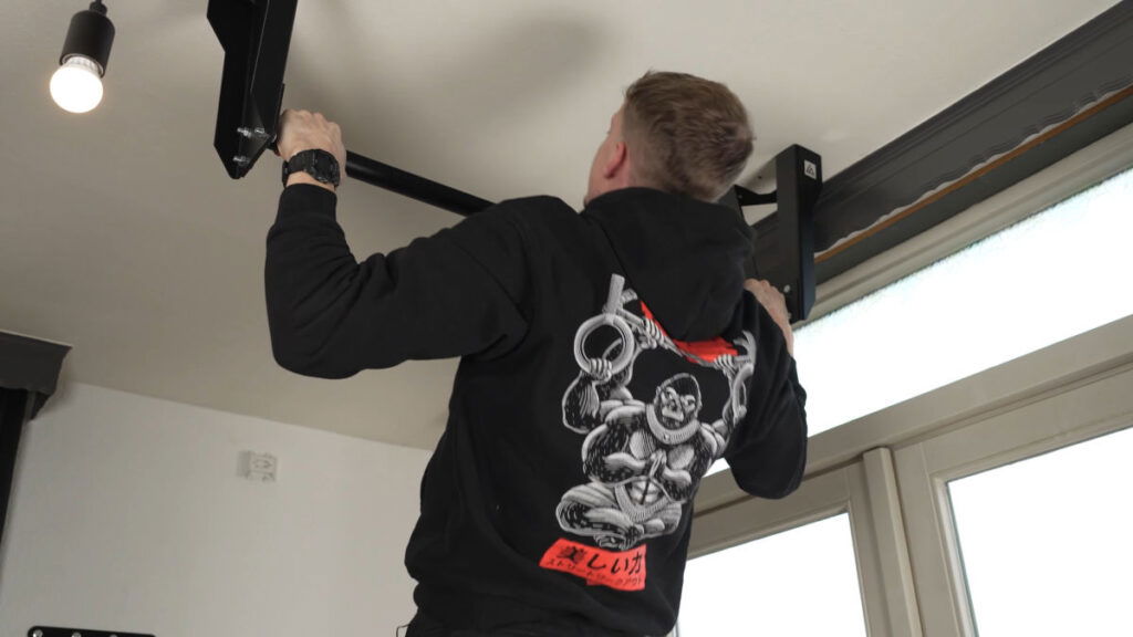 Man in black shirt with a gorilla picture on it performing a Wide Pull-Up on the Caliathletics Ceiling Pull-Up Bar.