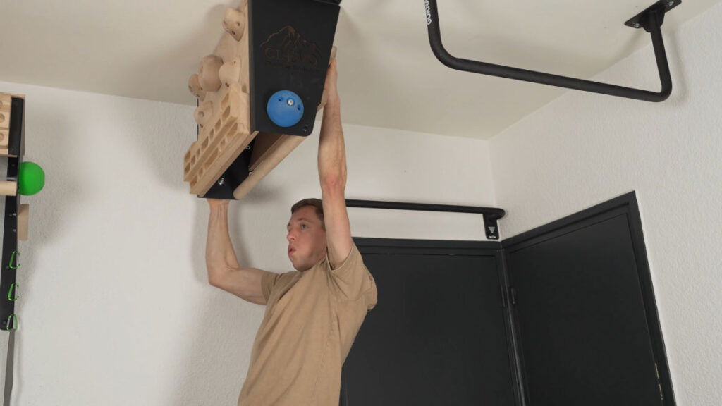 Man in beige shirt practicing climbing using the CLEVO Ceiling M and showing physical exertion.