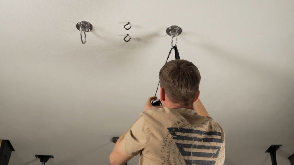 Man in beige shirt hanging the straps for Gymnastic Rings off a pair of ceiling rings and ceiling hooks.