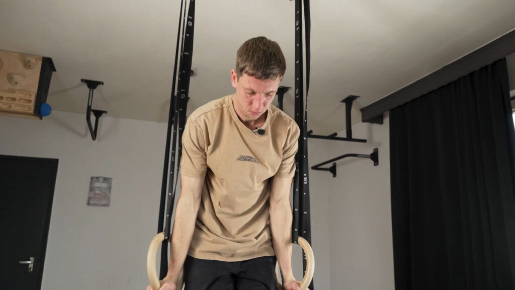 Man in beige shirt exercising using Gymnastic Rings suspended off ceiling rings.