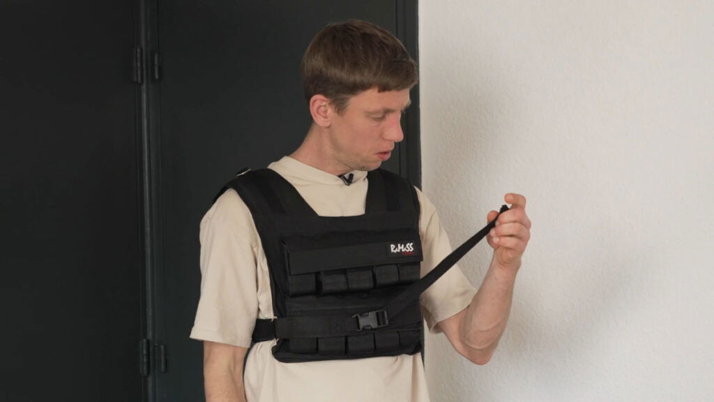 Man in white shirt inspecting the straps of the RaMaSS Fitness Weighted Vest he is wearing.