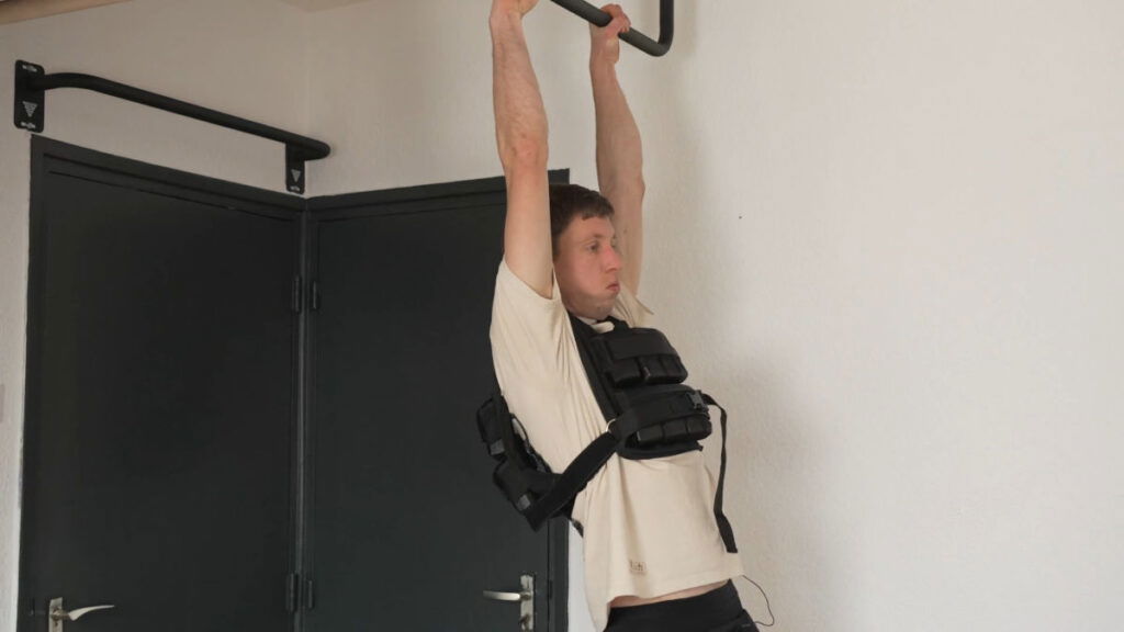 Man in white shirt hanging off a pull up bar wearing the RamaSS Fitness Weigthed Vest.