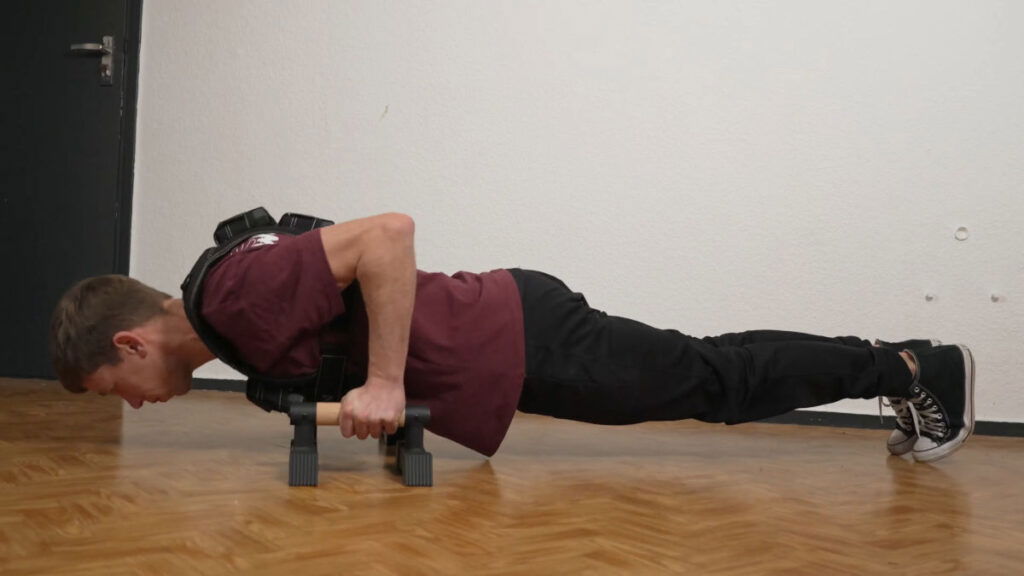 Man in red shirt doing push ups while wearing the Gravity Fitness Weighted Vest of 10kg with the assistance of a pair of Gravity Fitness parallettes.