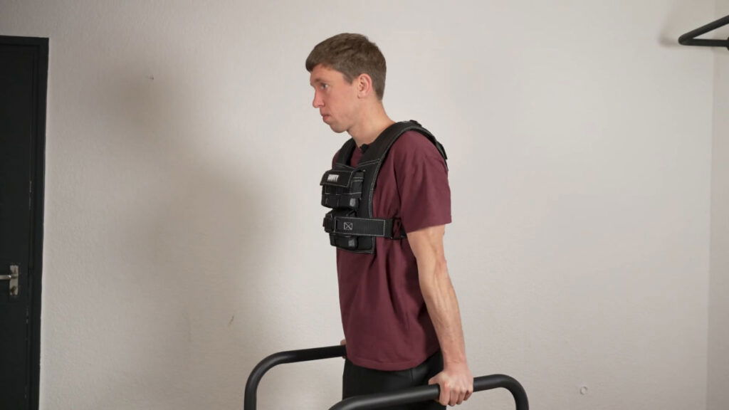 Man in red shirt doing dips while wearing the Gravity Fitness Weighted Vest of 10kg with the assistance of a pair of Gravity Fitness Dip Bars.