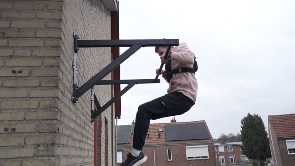 Man in white hoody attempting a muscle up while wearing the Gravity Fitness Weighted Vest of 10kg.