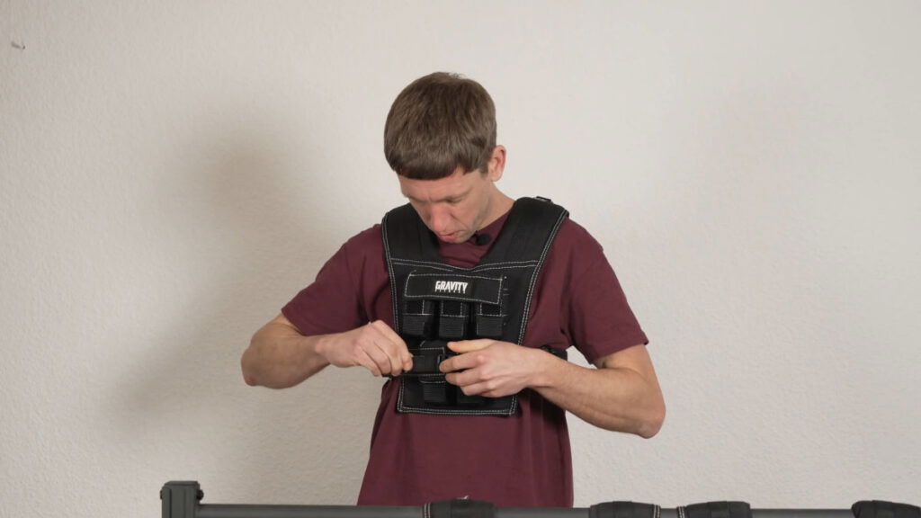 Man in red shirt putting on the 10kg Gravity Fitness Weighted Vest by fastening the buckle on the front.