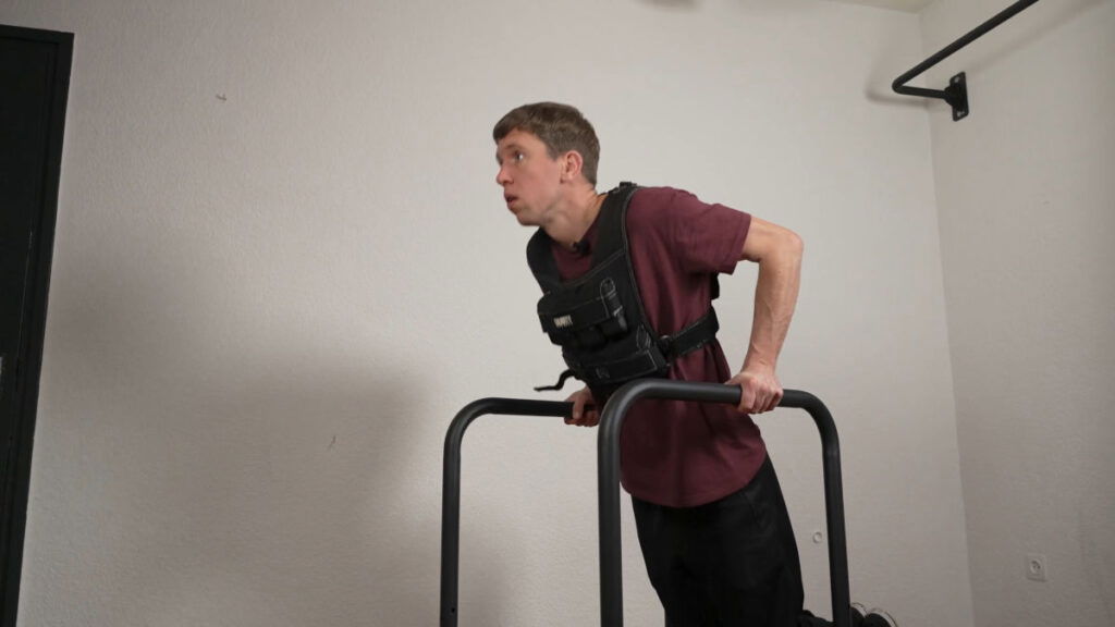 Man in red shirt doing dips while wearing the Gravity Fitness Weighted Vest of 20kg with the assistance of a pair of Gravity Fitness Dip Bars.