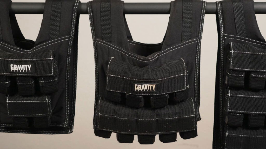 Gravity Fitness Weighted Vests close up hanging from a dip bar, showing the logo and thick fabric and stitching of the product.