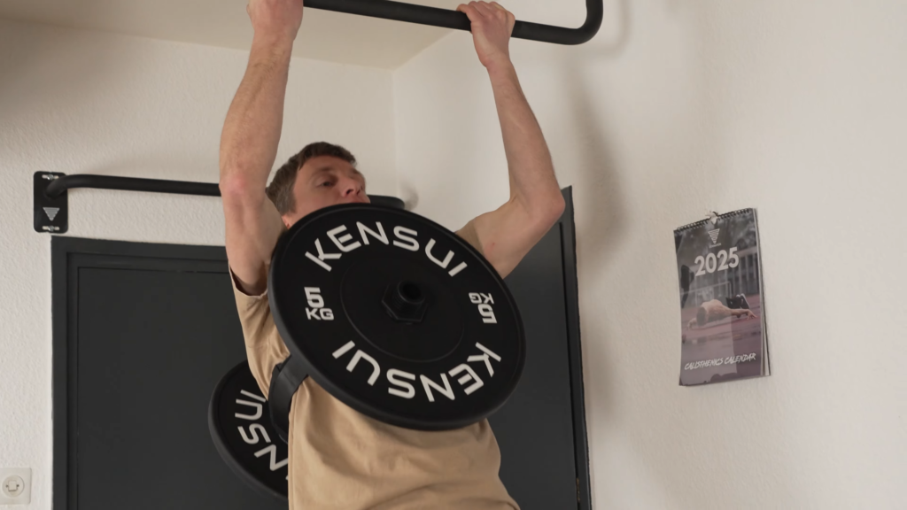 A man wearing a plate loaded weight vest has the front plate bump into his chin while he's doing a pull up.