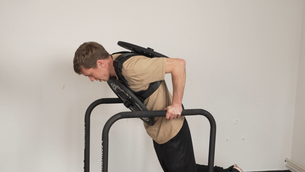 Side view of a man trying to do a dip while wearing a plate loaded weight vest and finding the back plate wedging against his elbows.