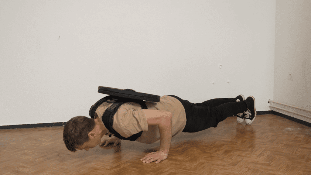 Man successfully doing push ups while wearing a plate loaded weight vest with two plates attached to the back and no plates on the front.