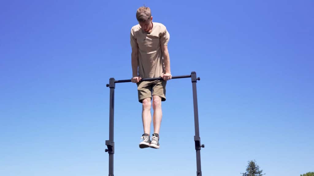 Man in beige shirt doing a muscle-up on the Eric Flag Free-Standing Pull-Up Bar