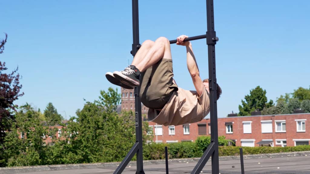 Man in beige shirt doing a tucked front lever on the Eric Flag Free-Standing Pull-Up Bar in its lowest bar setting.