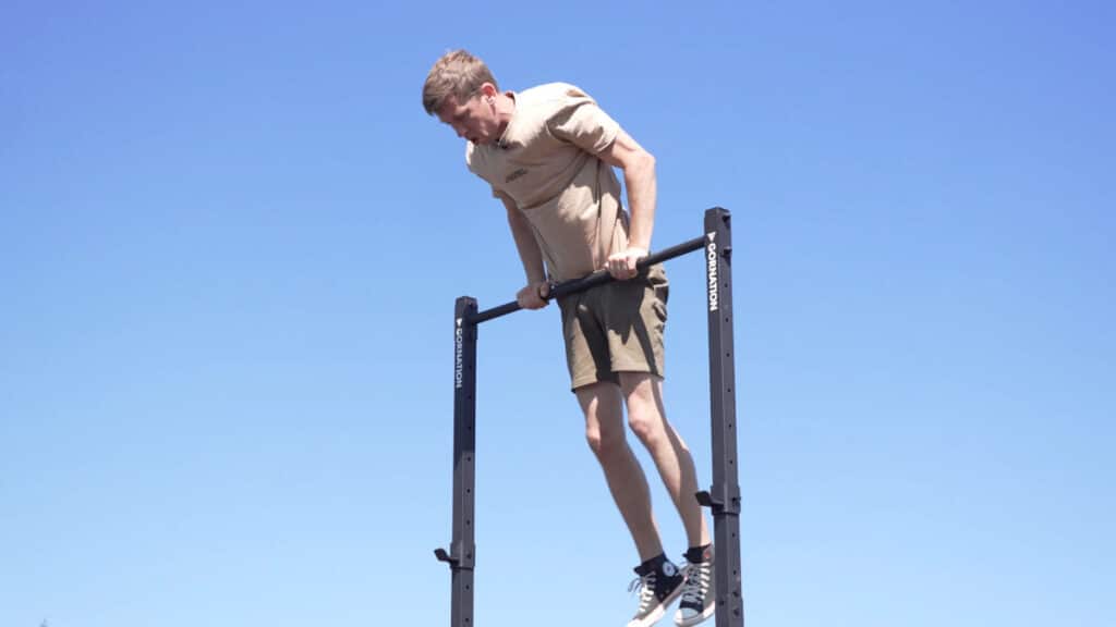Man in beige shirt doing a muscle-up on the Gornation Pull-Up Station Free-Standing Pull-Up Bar.