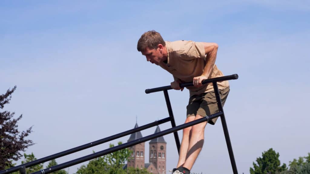 Man in beige shirt doing a muscle-up on the Gravity Fitness Free-Standing Pull-Up Bar turned on its side.