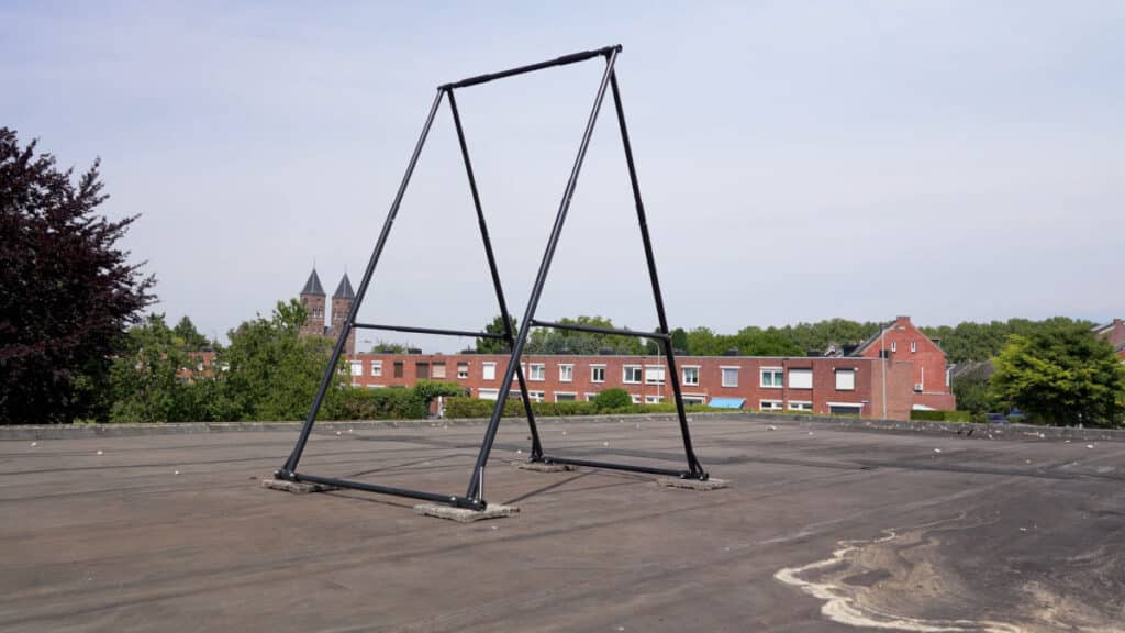 The Khanh Trinh Foldable Free-Standing Pull-Up Bar standing on a roof with a housing block in the near background and a church in the far background.