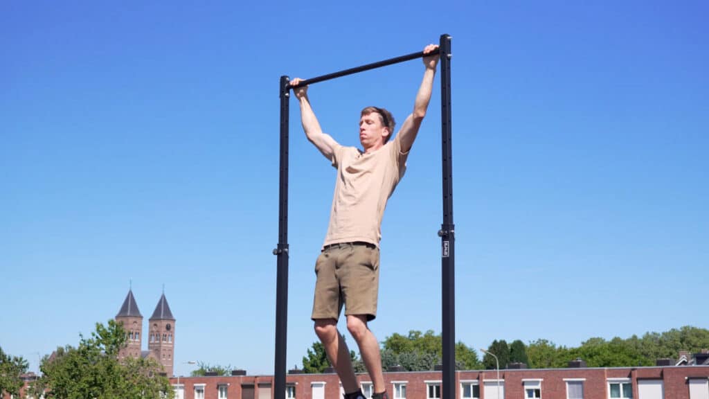 Man in beige shirt doing a wide pull-up on the RaMass Fitness Free-Standing Pull-Up Bar.