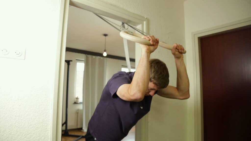 Man in violet shirt performing pelicans with the Gorletic Gymnastic Rings suspended in a doorway.