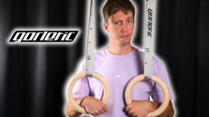 Man in lavender shirt standing between two Gorletic Gymnastic Rings resting his hands through them.