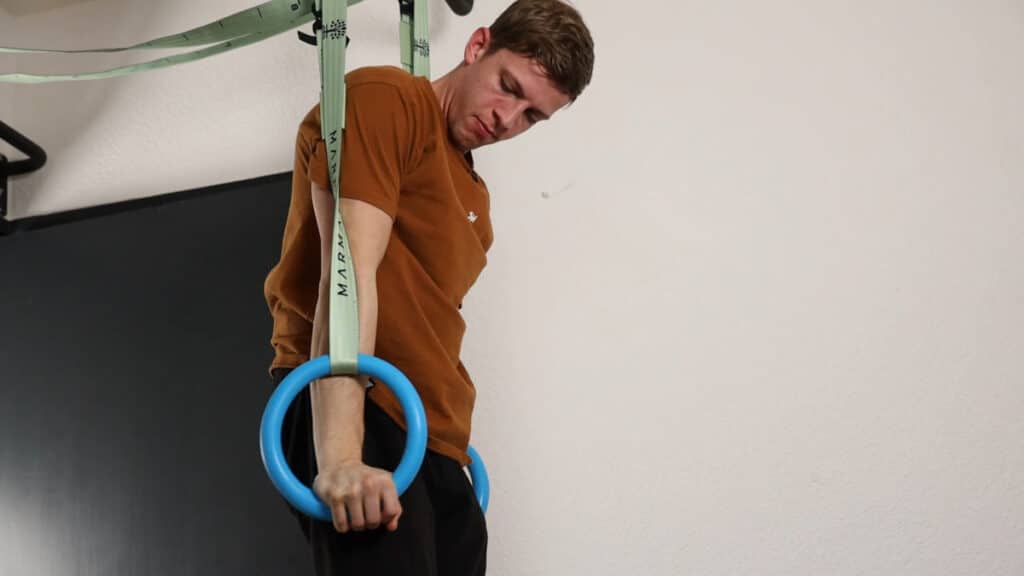 Man in orange shirt completing a Muscle Up on the Infinity Rings.