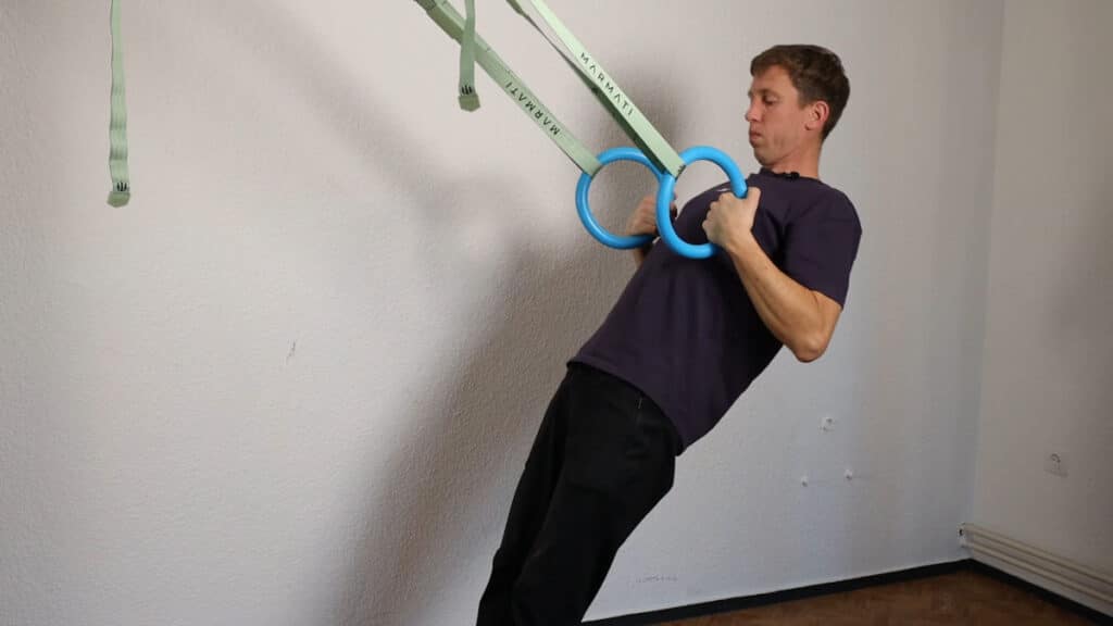 Man in purple shirt performing body rows on the Infinity Rings.