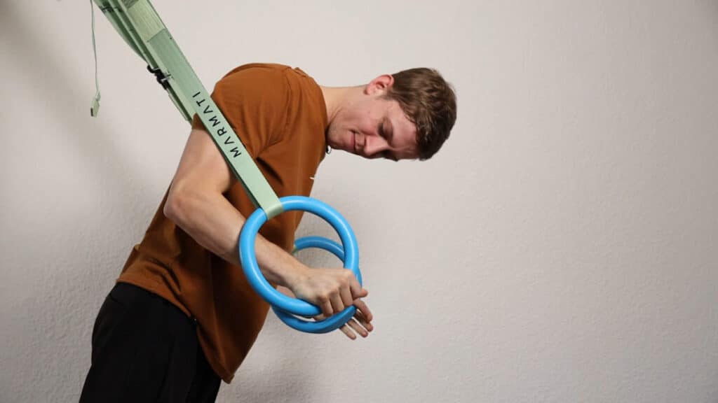 Man in orange shirt performing Australian Push-Ups on the Infinity Rings and checking his technique carefully.
